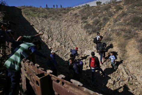 在墨西哥的蒂华纳市，洪都拉斯移民星期日越过美国边境围墙，前往加利福尼亚州的圣迭戈，然后向山顶的美国边境巡逻队自首。（美联社）
