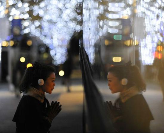 在日本东京，一名女郎在挂满圣诞灯饰的街头。（新华社）