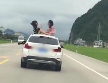 中国两名女子去年坐在一辆行驶中的休旅车车顶，在广西的公路上玩猜拳。（微博视频截图）