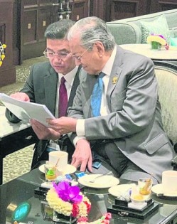 东盟峰会开始前， 经济事务部长拿督斯里阿兹敏蹲在首相敦马哈迪身旁， 讨论汇报细节。