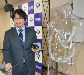 大阪大学团队医生堂前圭太郎讲解从耳后伸出的电线连接左手所持的体外装置，让装在心脏上的血泵运转。（互联网图） 